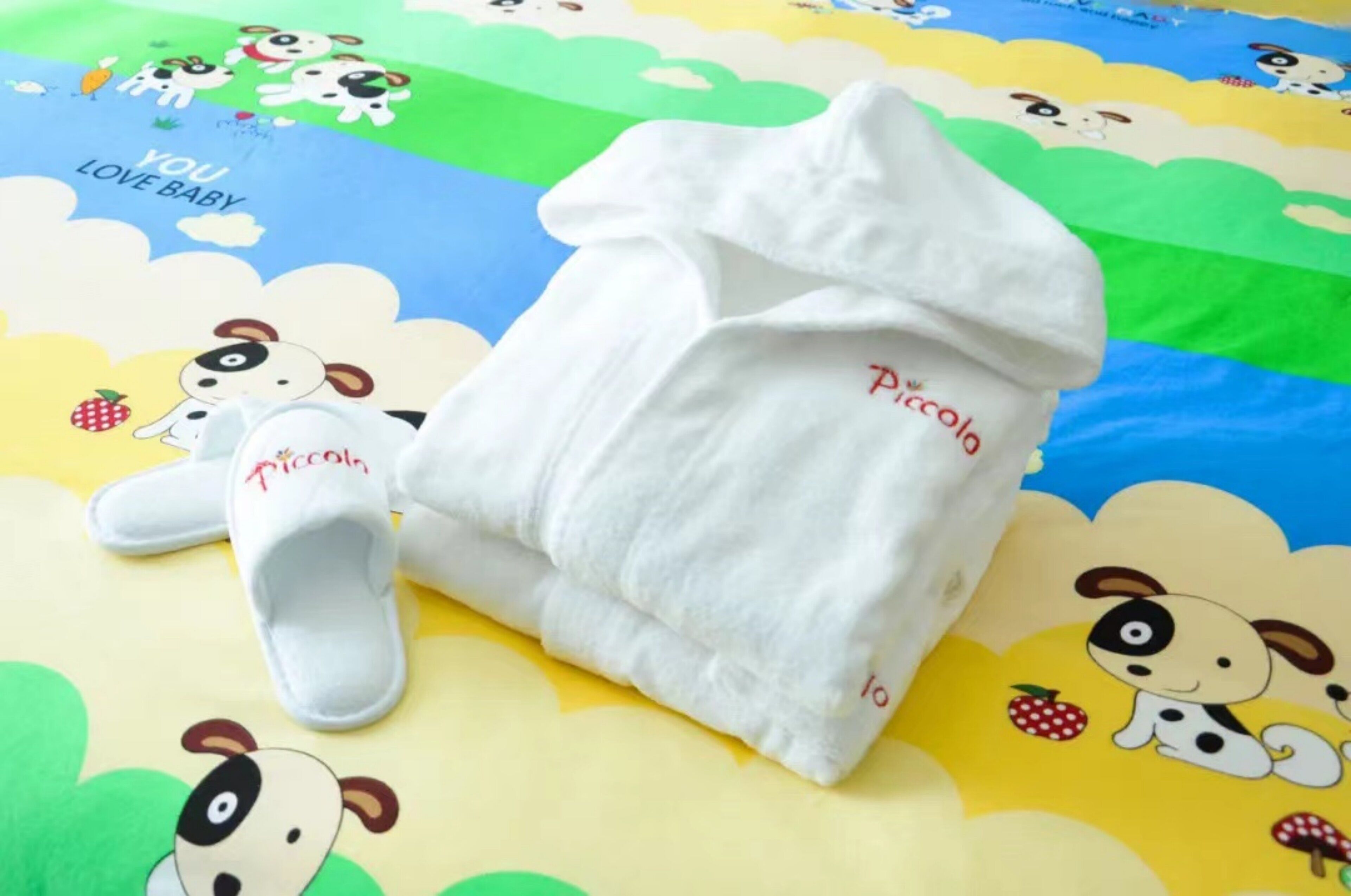A baby blanket with a dog design and the word 'Piccolo' on it, placed on a colorful bedspread with similar dog patterns.