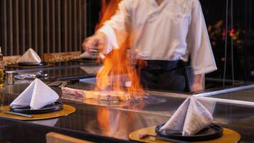 A chef grilling meat on a high table with a clear view of the cooking process.