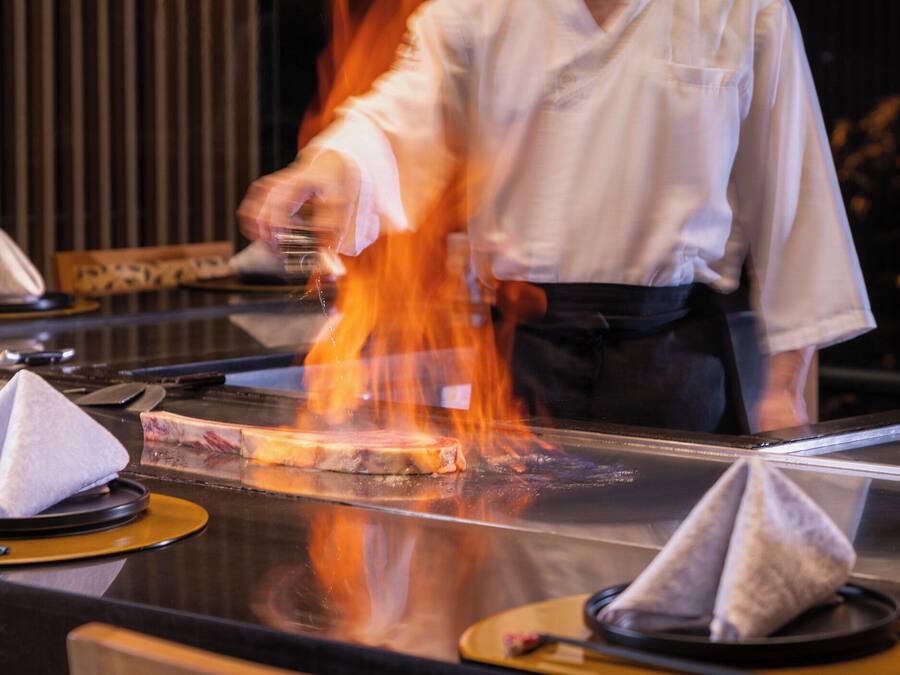 A chef grilling meat on a high table with a clear view of the cooking process.