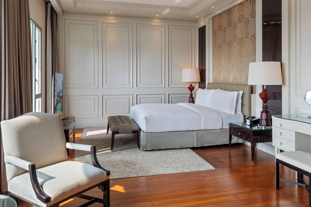 A hotel room with a large bed, a desk, a chair, and a mirror.