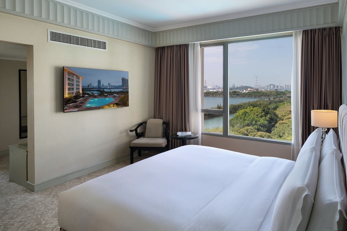 A hotel room with a large bed, a chair, a table, and a painting of a cityscape.