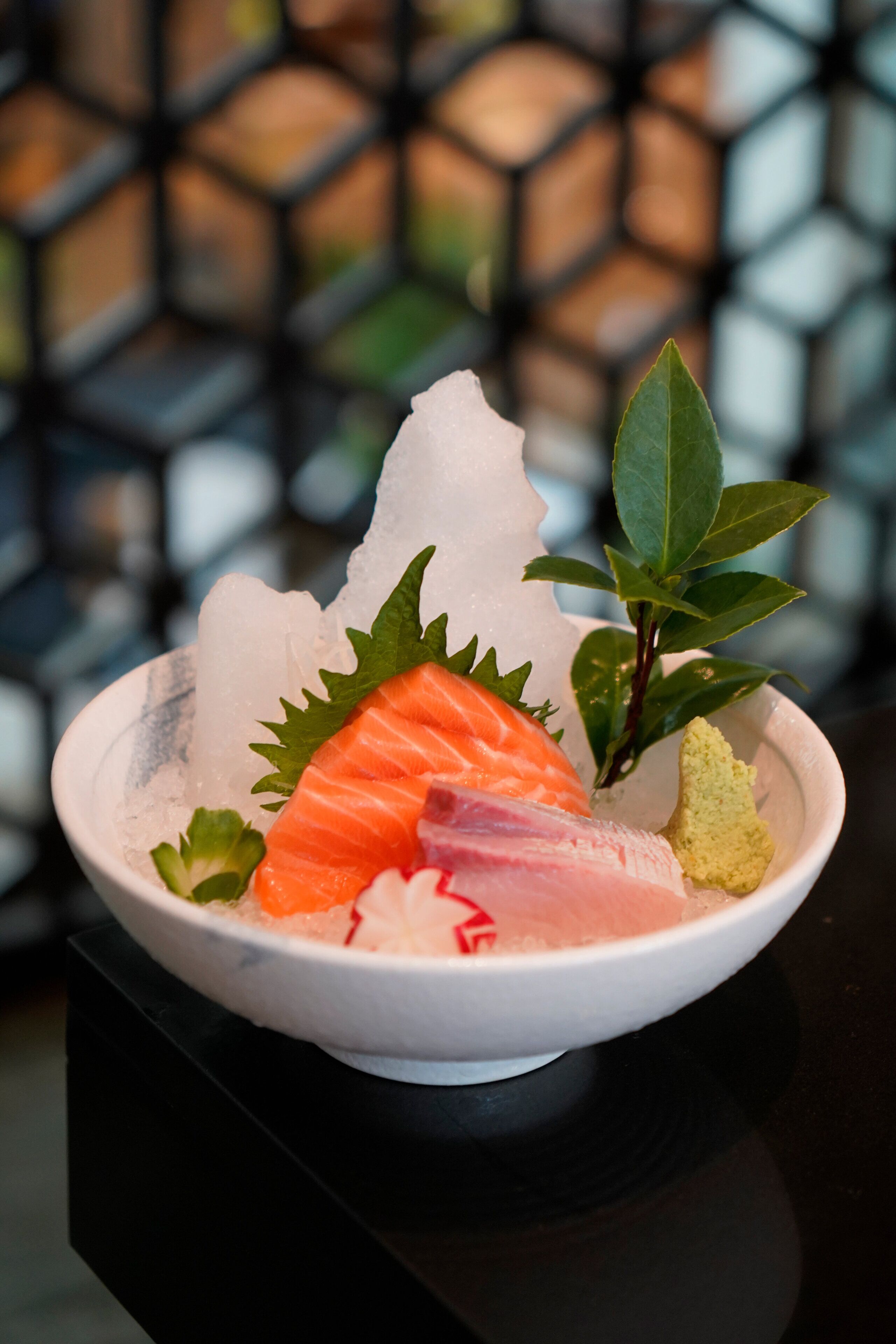 A bowl of sashimi with ice and garnishes on a black table.