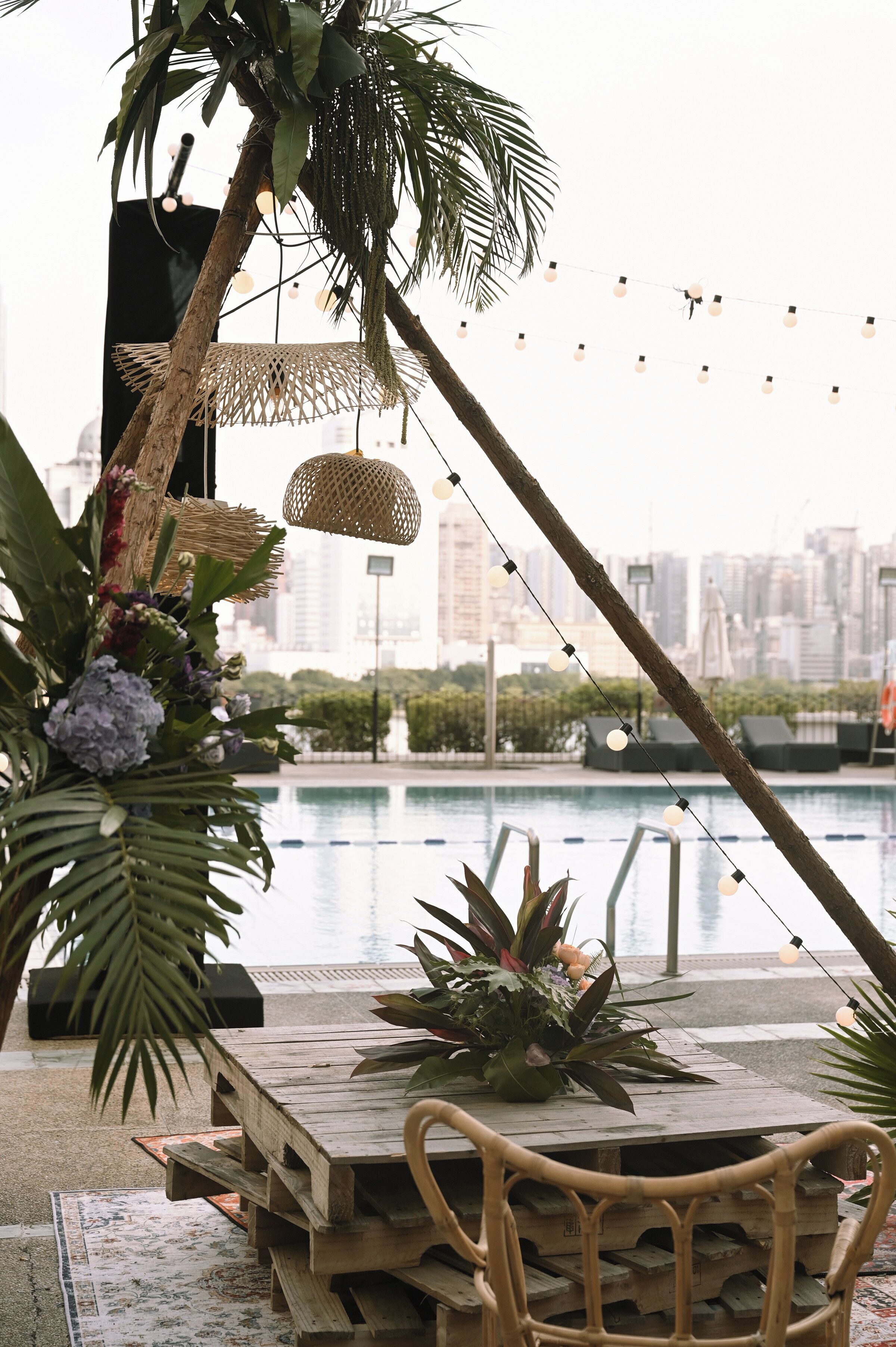 An outdoor dining area with a view of a city skyline, a pool, and string lights.