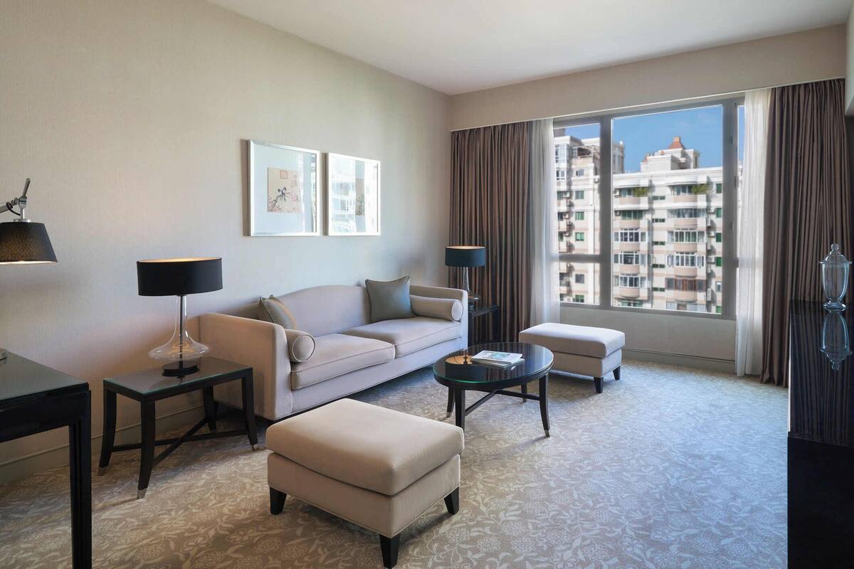 A modern hotel room with a sofa, armchair, coffee table, and a TV.