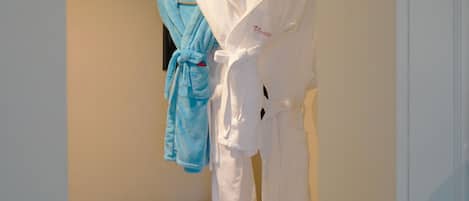 A hotel room with a bed, a small table with slippers, and two robes hanging on a rack.