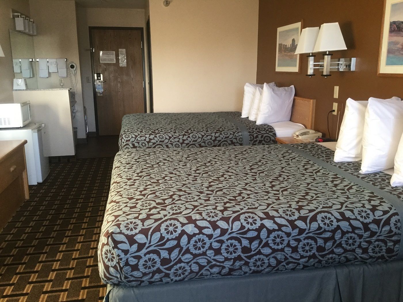 A hotel room with two beds, a desk, a microwave, and a door leading to a bathroom.