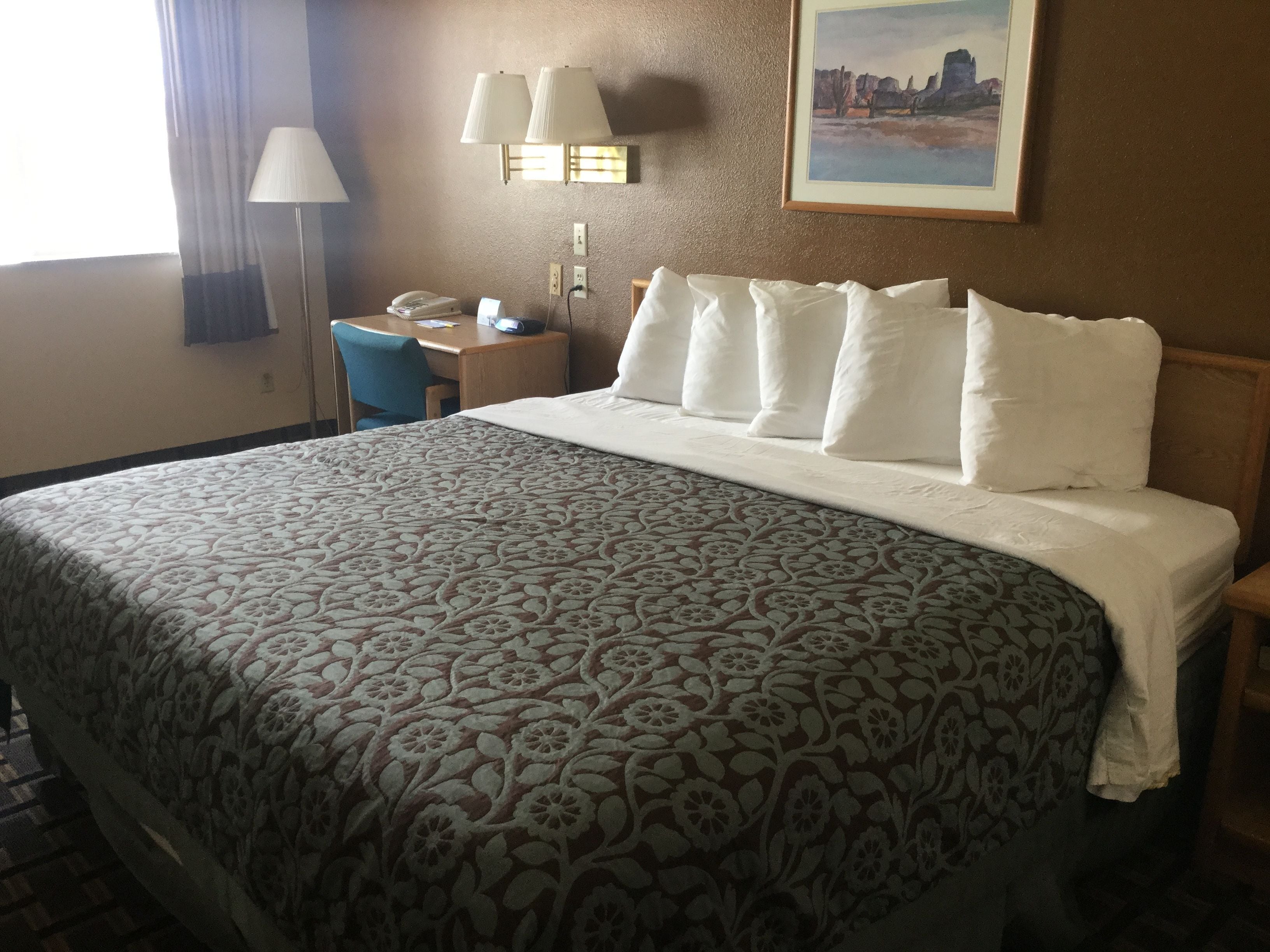 A hotel room with a large bed, a desk with a telephone, and two wall-mounted lamps.