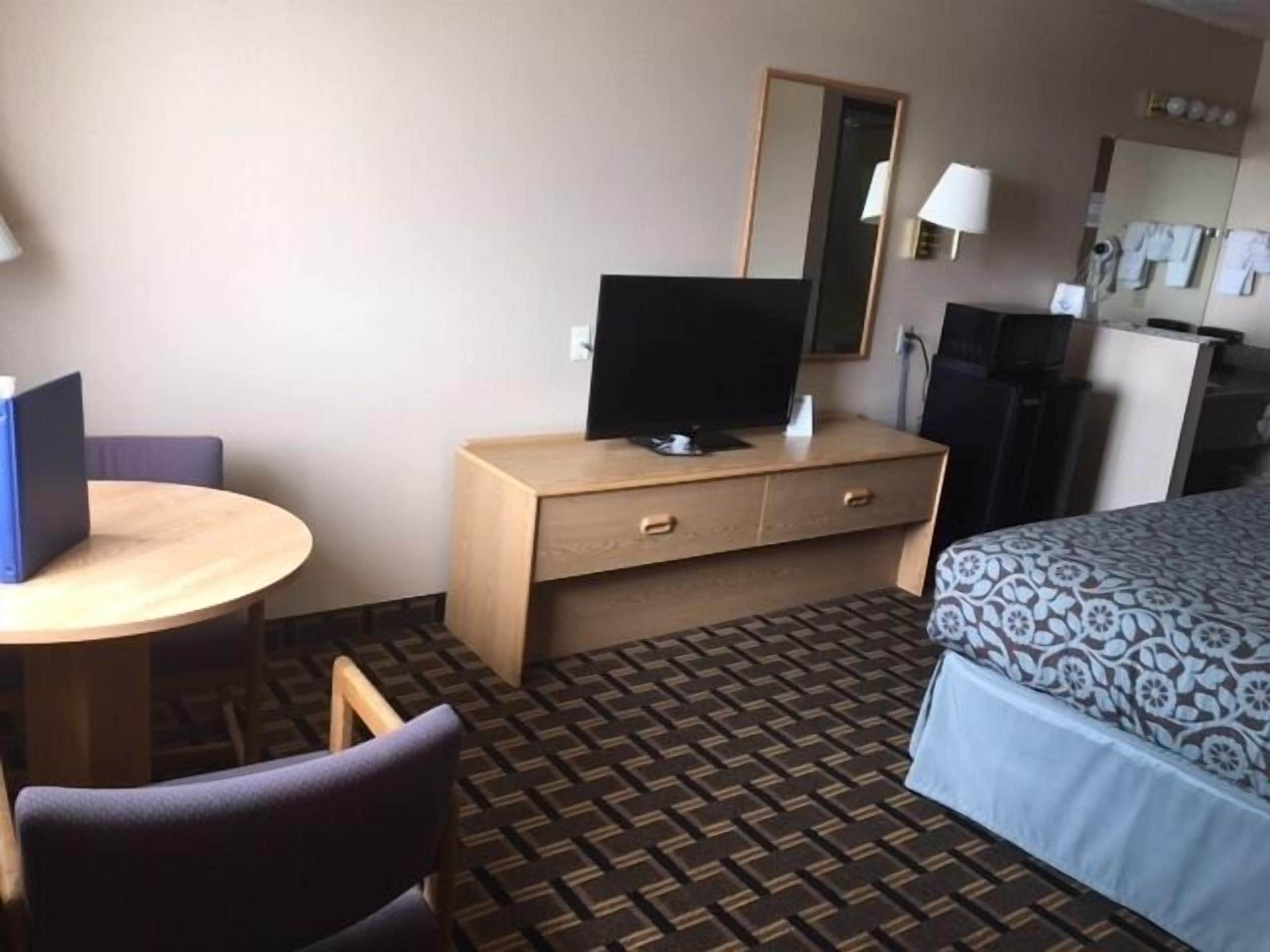 A hotel room with a bed, a desk with a computer, a chair, a dresser, and a patterned carpet.