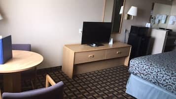 A hotel room with a bed, a desk with a computer, a chair, a dresser, and a patterned carpet.