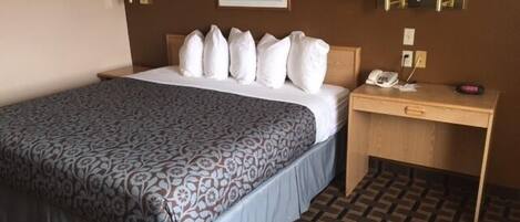 A hotel room with a bed, a desk with a telephone, and two wall-mounted lamps.