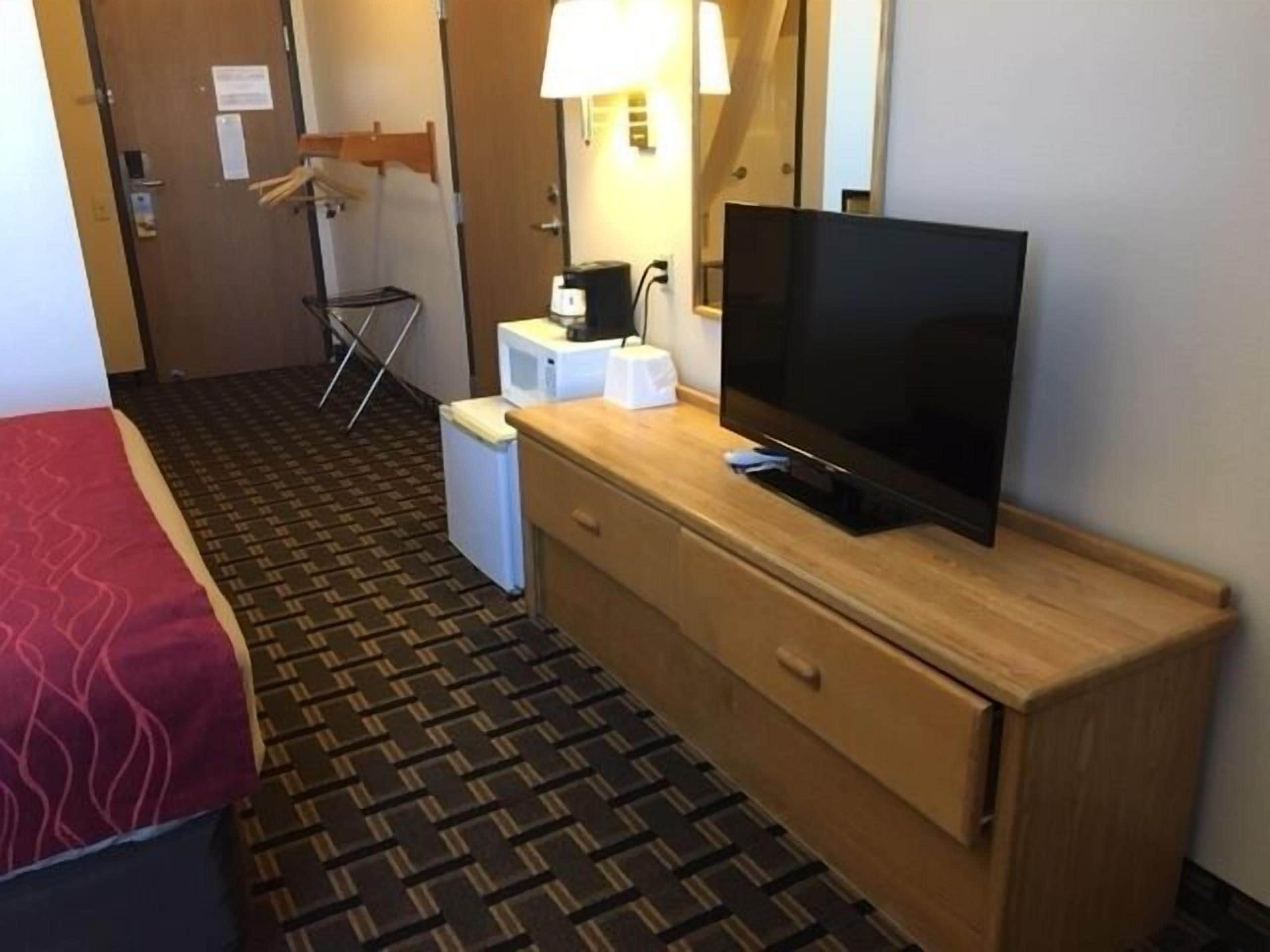 Ein Hotelzimmer mit einem Bett, einem Fernseher auf einer Holzkommode, einer Mikrowelle und einem kleinen Kühlschrank.