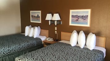 Habitación de hotel con dos camas, cada una con ropa de cama estampada, una mesita de noche con lámpara y dos cuadros en la pared.