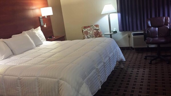 A hotel room with a large bed, two bedside lamps, a chair, and a heater. - Baymont by Wyndham Paducah (Paducah)