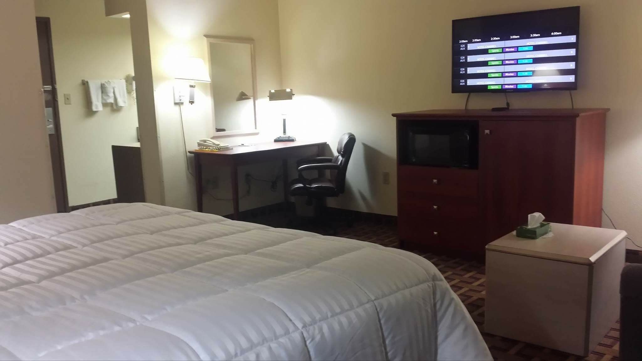 A hotel room with a bed, a desk with a chair, a television, and a small cabinet.