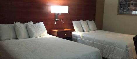 A hotel room with two single beds, a nightstand, a wall-mounted lamp, and a framed picture on the wall.