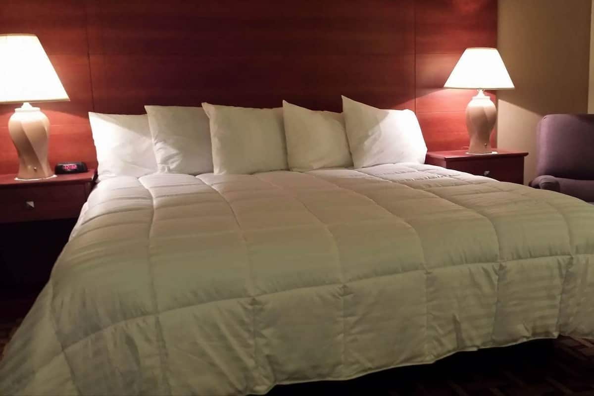 A hotel room with a large bed, two bedside tables with lamps, a chair, and a wooden headboard.