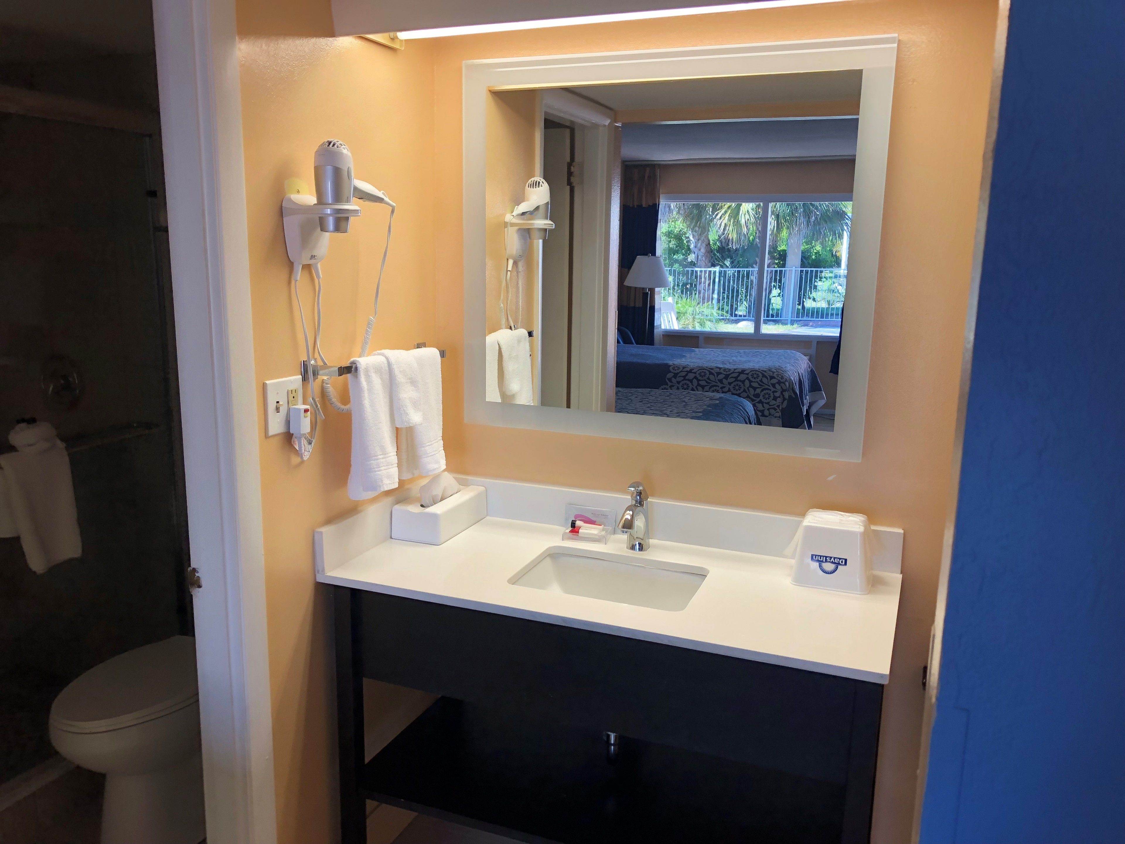 Een badkamer met een witte wasbak, een spiegel en een aan de muur bevestigde haardroger.