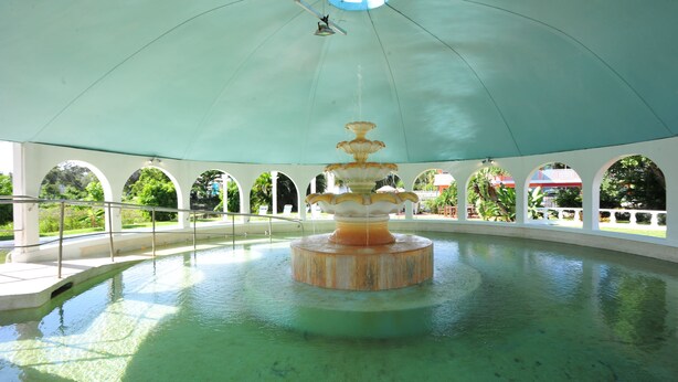 A large indoor pool with a central fountain, surrounded by white arches and a green canopy. - Days Inn by Wyndham Fort Myers Springs Resort (Fort Myers)