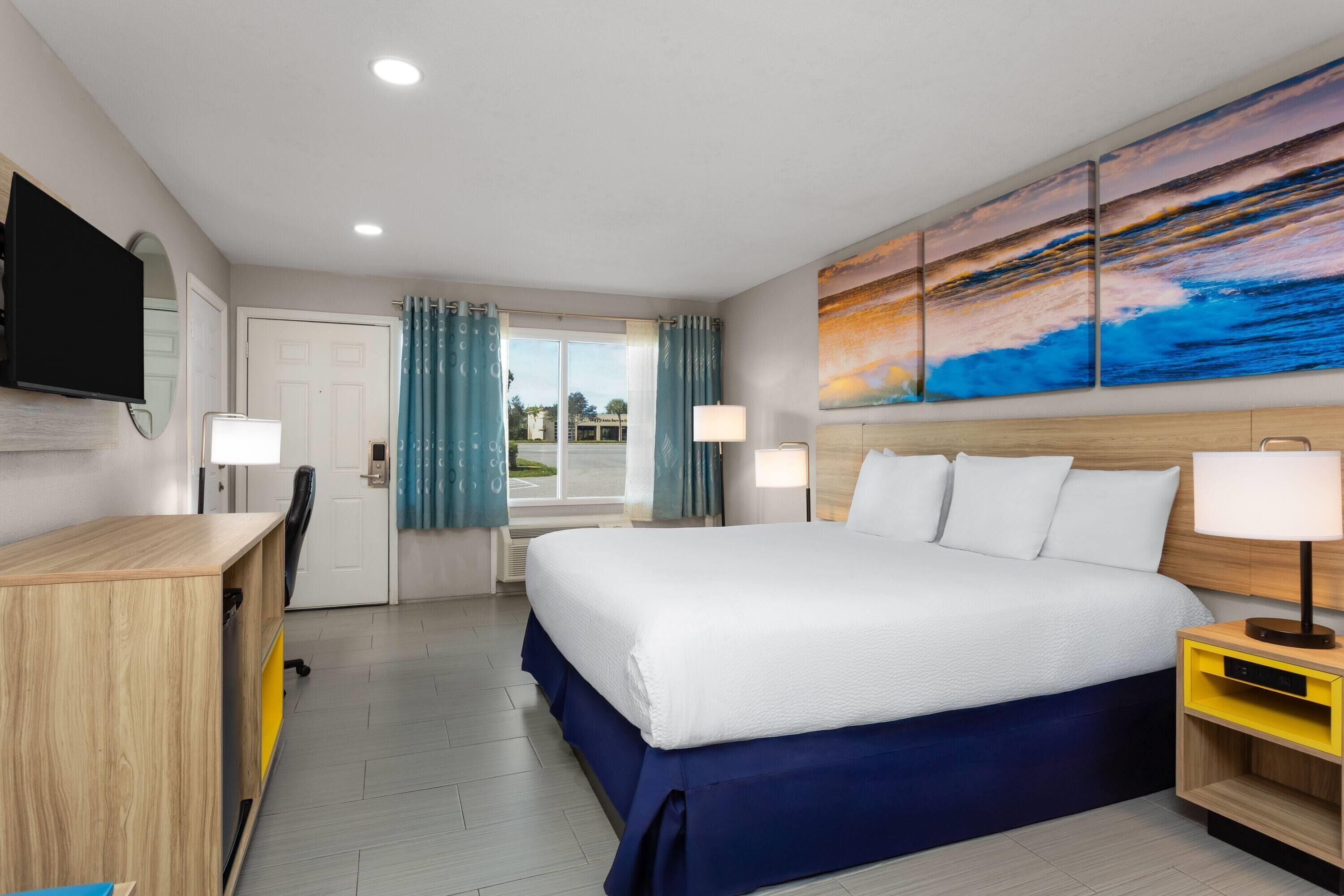 A hotel room with a large bed, a desk, a TV, and a painting on the wall.
