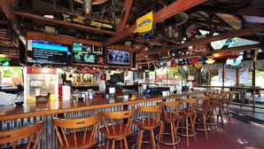 A bar area with wooden chairs, a popcorn machine, and multiple televisions displaying news. - Days Inn by Wyndham Fort Myers Springs Resort (Fort Myers)