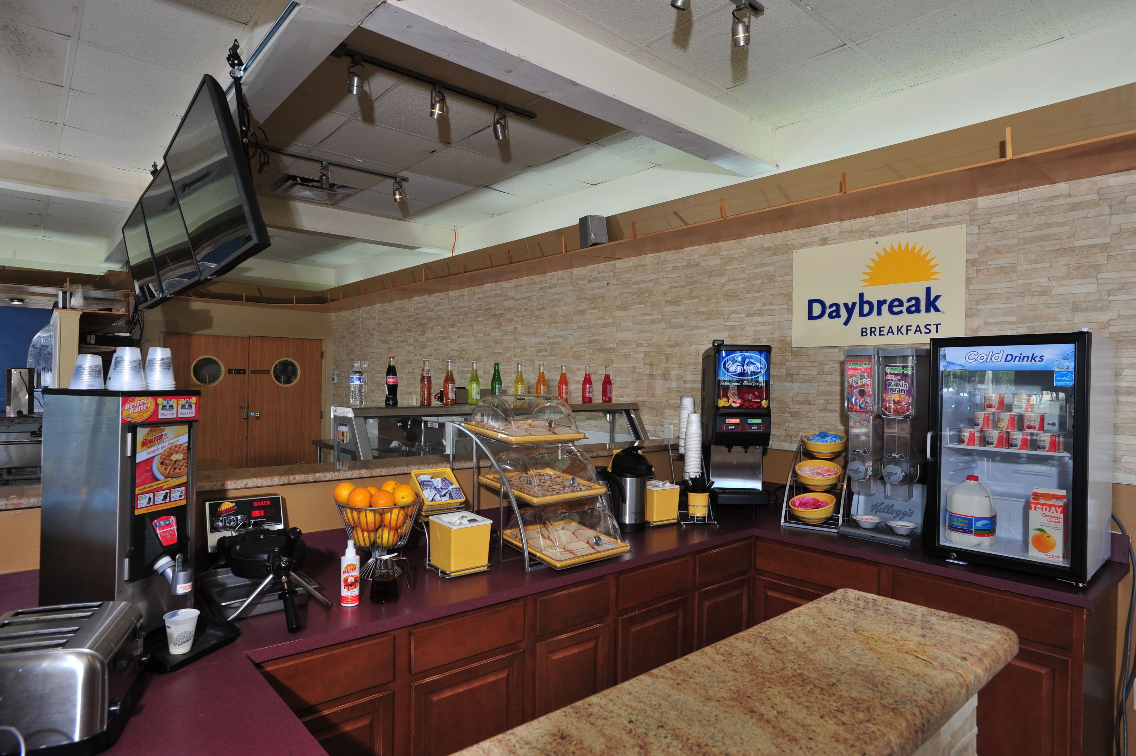 Un comptoir pour prendre le petit-déjeuner, avec une enseigne indiquant « Petit-déjeuner Daybreak », une machine à café, un réfrigérateur rempli de boissons fraîches et divers produits alimentaires.