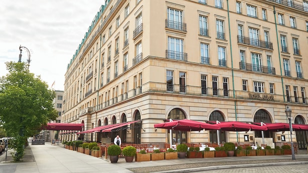 A large hotel with multiple floors, outdoor seating with red umbrellas, and a well-maintained garden area. - Hotel Adlon Kempinski (Berlin)