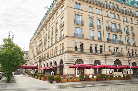 A large hotel with multiple floors, outdoor seating with red umbrellas, and a well-maintained garden area.