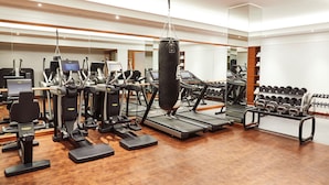 Un gimnasio moderno con cintas de correr, máquinas elípticas, un saco de boxeo y un estante con mancuernas.