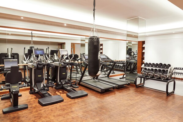 A modern gym with treadmills, elliptical machines, a punching bag, and a rack of dumbbells. - Hotel Adlon Kempinski (Berlin)