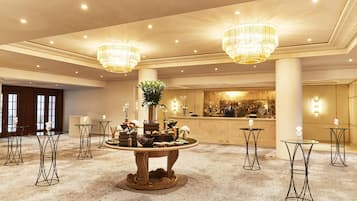 Vestíbulo de hotel con mostrador de recepción, candelabros, una mesa redonda con comida y piso alfombrado.