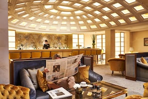 A hotel lobby with a bar area, seating, and a ceiling with skylights.