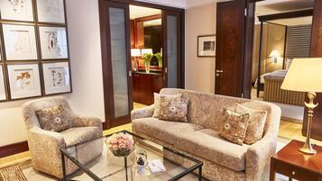 Habitación de hotel con sofá, sillón y una mesa de centro de vidrio con un centro de mesa floral.