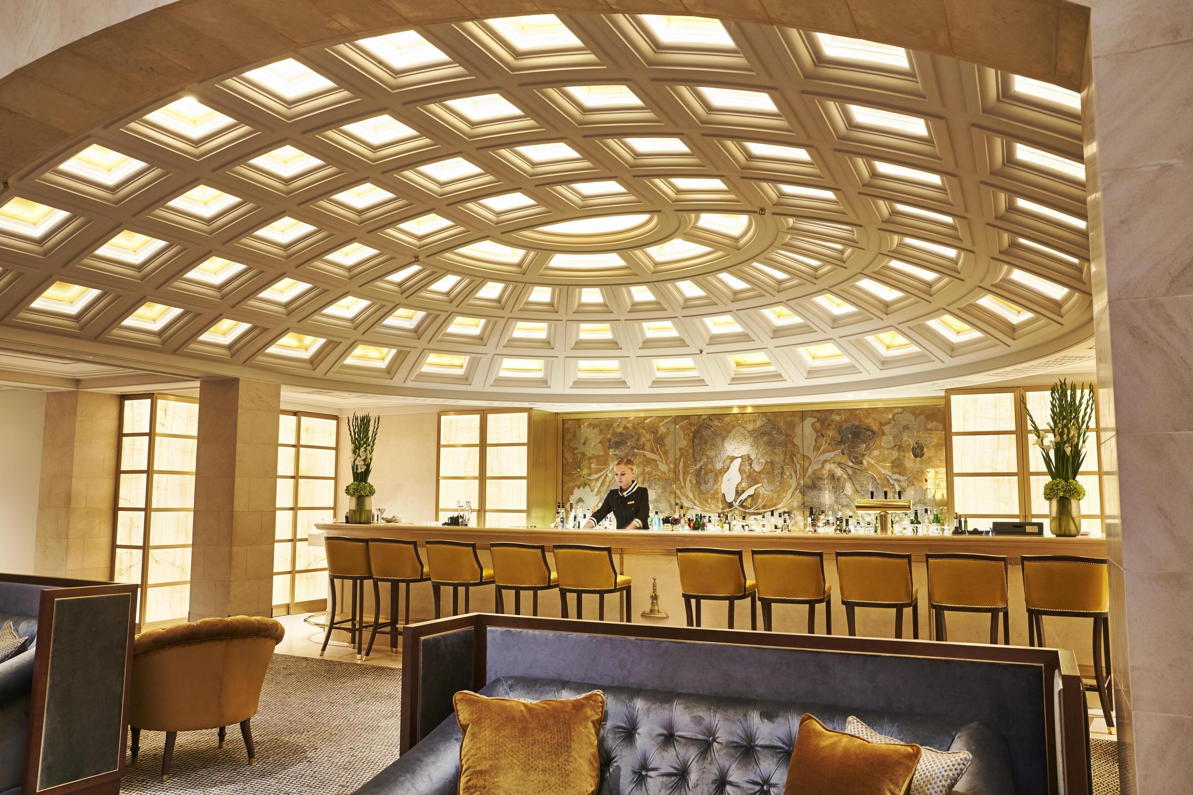 En hotellobby med en bardel, sittplatser och ett högt tak med takfönster.
