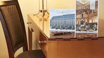 A hotel room with a wooden desk, a chair, a lamp, and a framed picture of a building with the word 'BERLIN' on it.