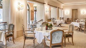 Un restaurante con varias mesas y sillas, elegantes lámparas de araña y un suelo con diseño de ladrillo.