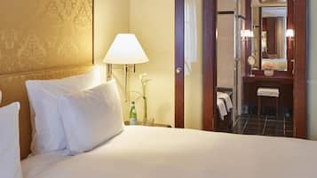 A hotel room with a bed, a lamp, a bottle, and a mirror.