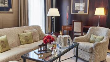Ein Zimmer mit einer Couch, Sesseln, einem Couchtisch, einer Lampe, einer Blumenvase und einer Champagnerflasche.