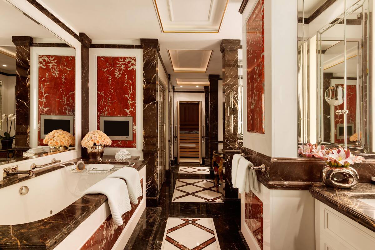 A luxurious bathroom with a large bathtub, marble walls, and a mirror.