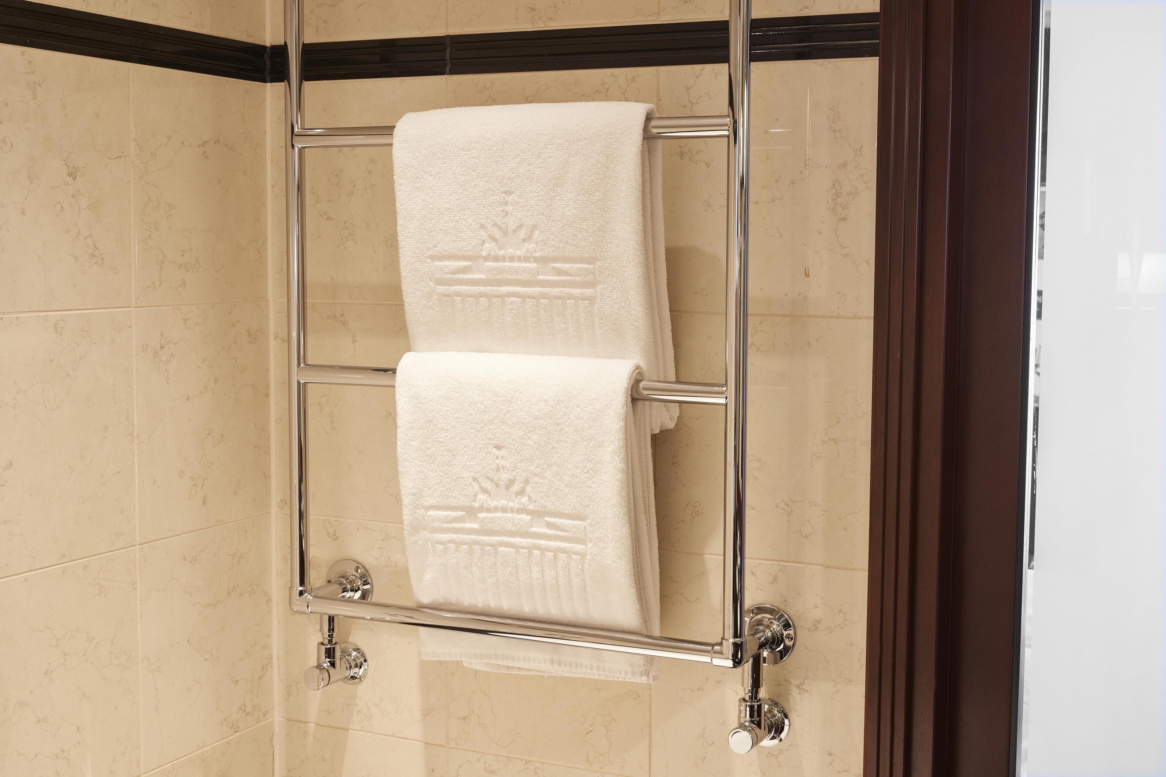 Ein Badezimmer mit Duschabtrennung aus Glas, einem chromfarbenen Handtuchhalter mit zwei Handtüchern und Marmorfliesen.