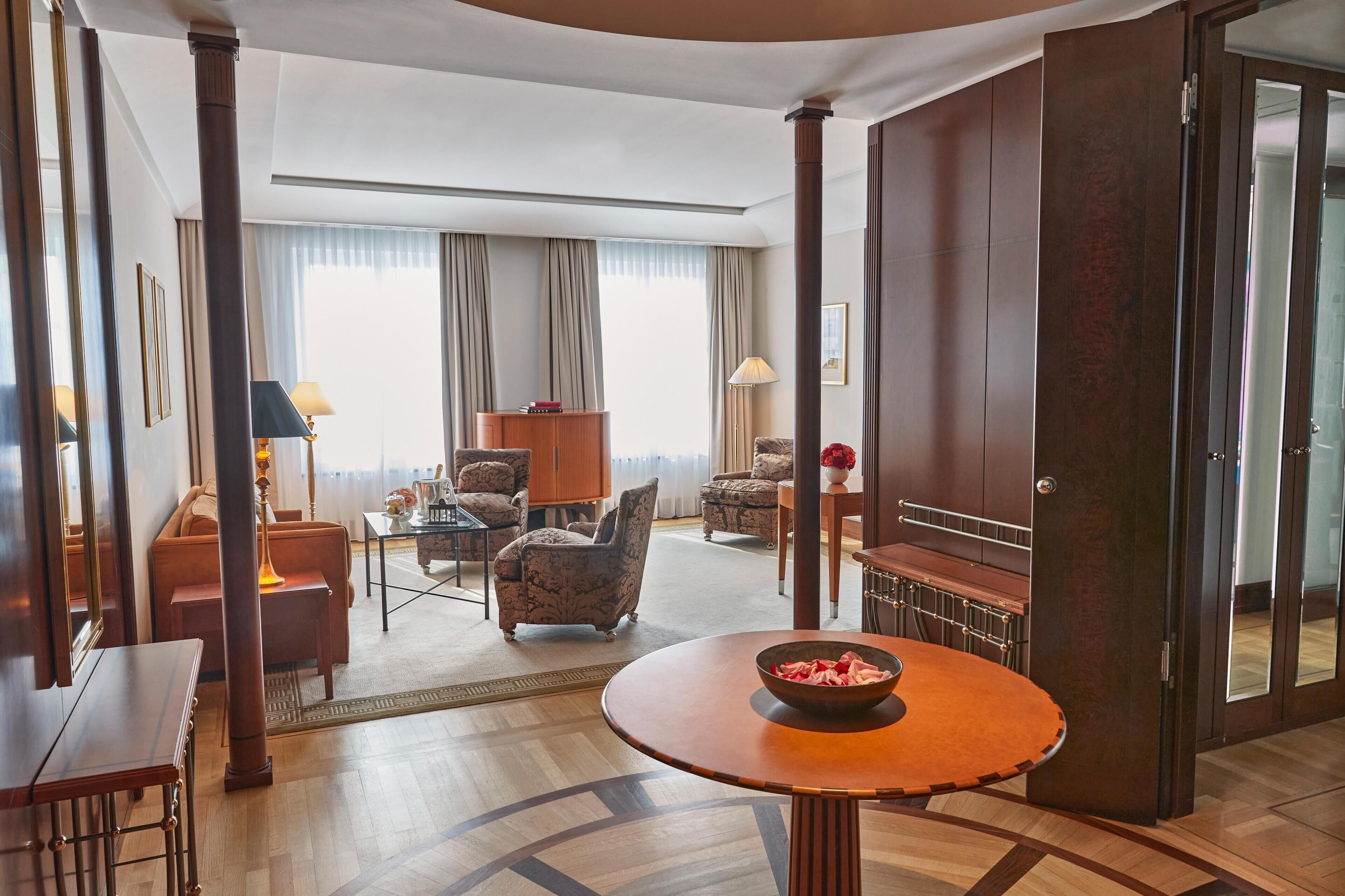 Habitación de hotel con piso de madera, una mesa redonda con un tazón, un sofá, una silla, un escritorio y un armario.