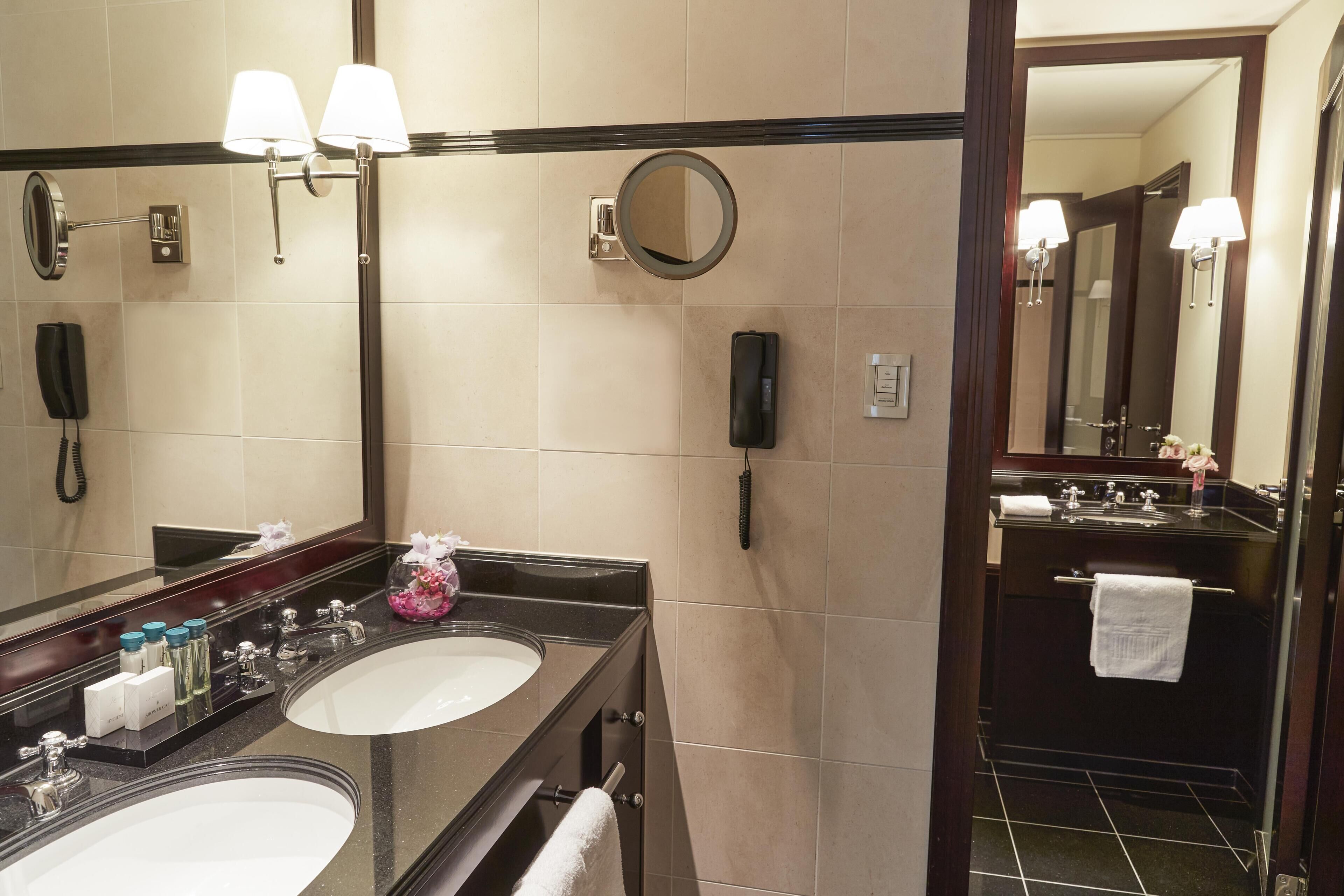 Ett hotellbadrum med två handfat, en spegel, en telefon och en handdukshängare.