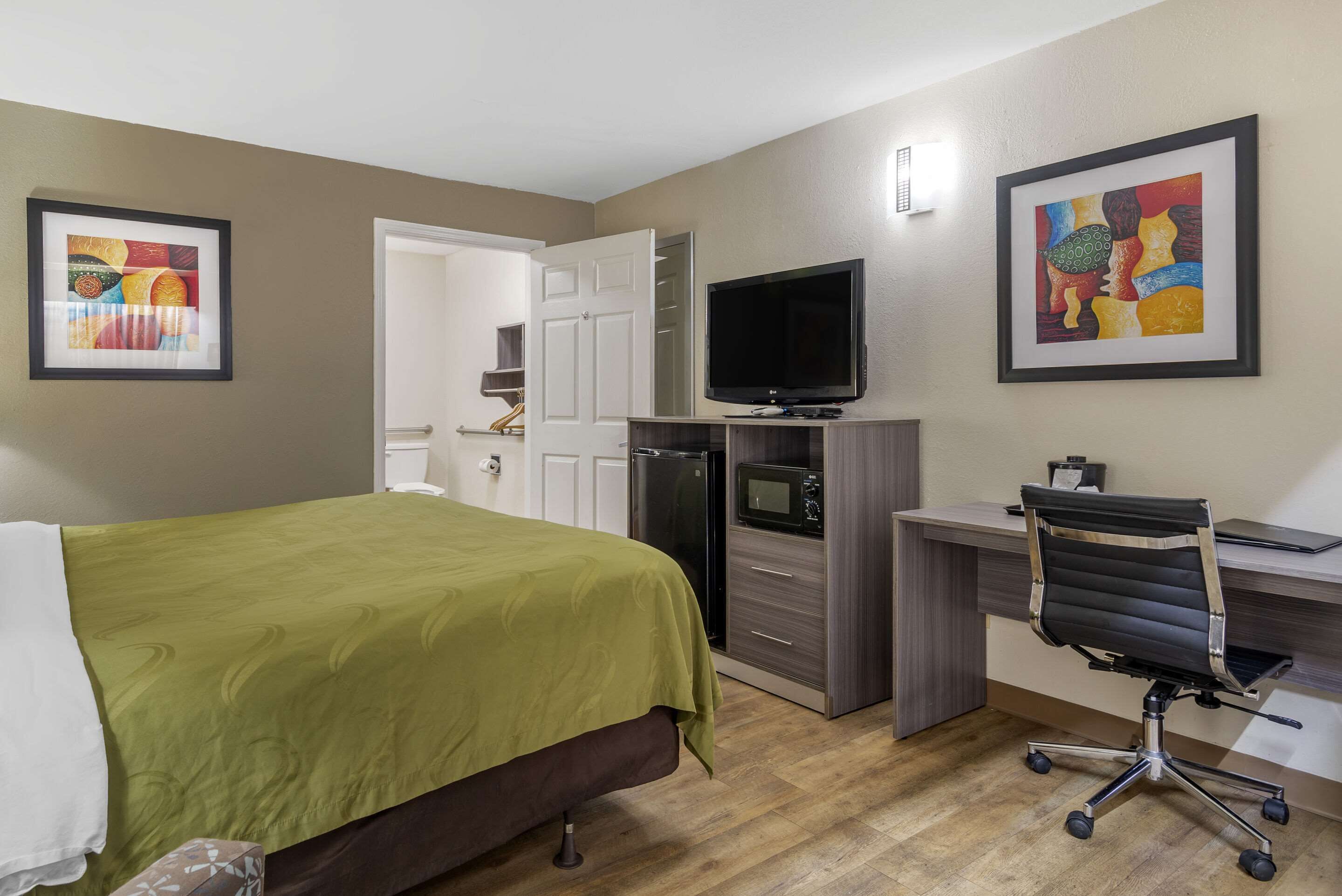 Ein Hotelzimmer mit Bett, Schreibtisch, Stuhl, Fernseher und Bildern an den Wänden.