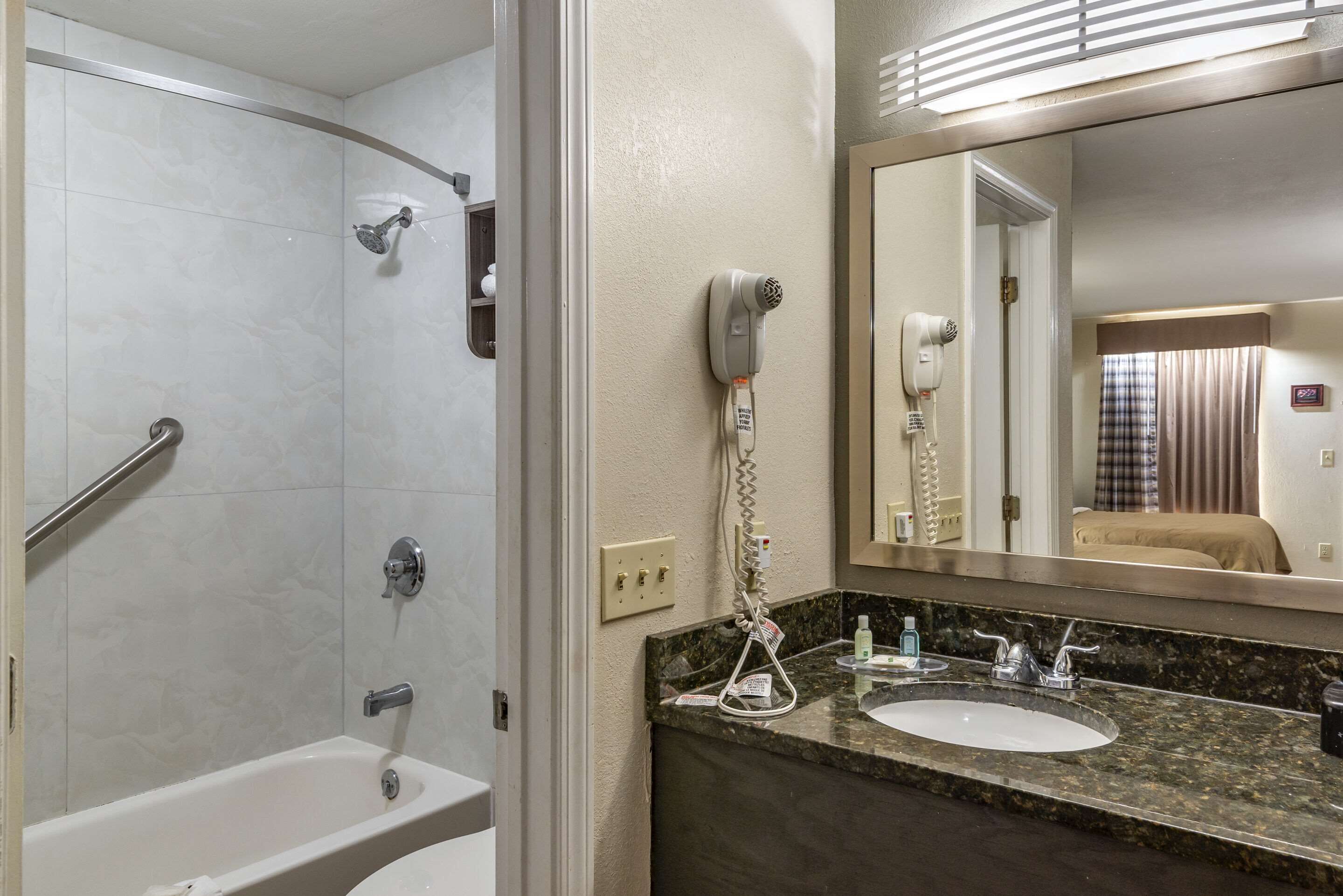A bathroom with a shower, a sink, and a hairdryer mounted on the wall.
