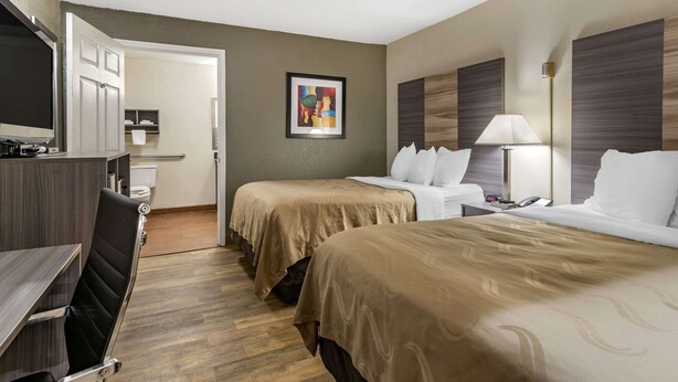 Hotelkamer met twee bedden, een bureau, een stoel, een televisie en een zichtbare badkamer door een geopende deur.