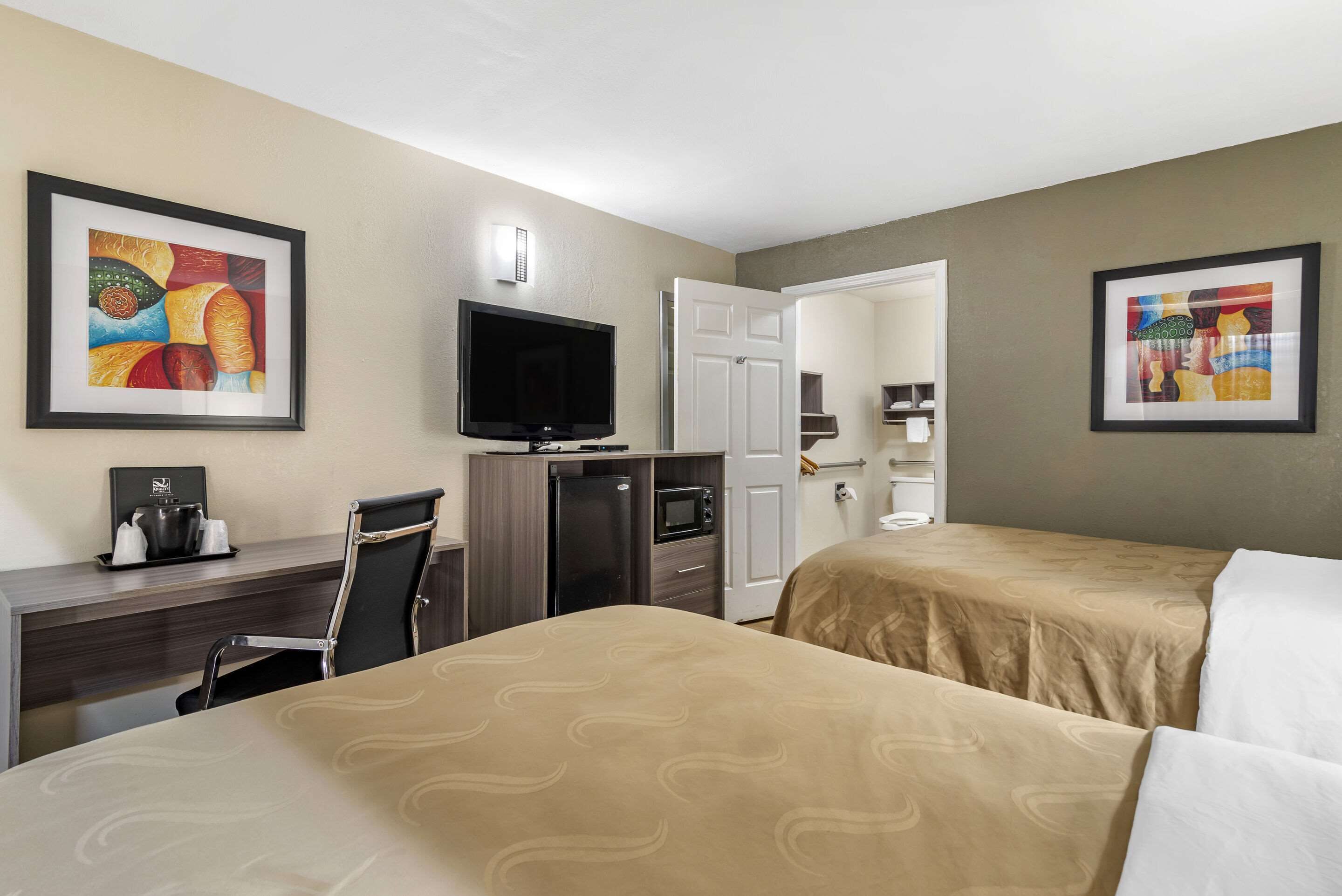 A hotel room with two beds, a desk with a TV, a minibar, and artwork on the walls.