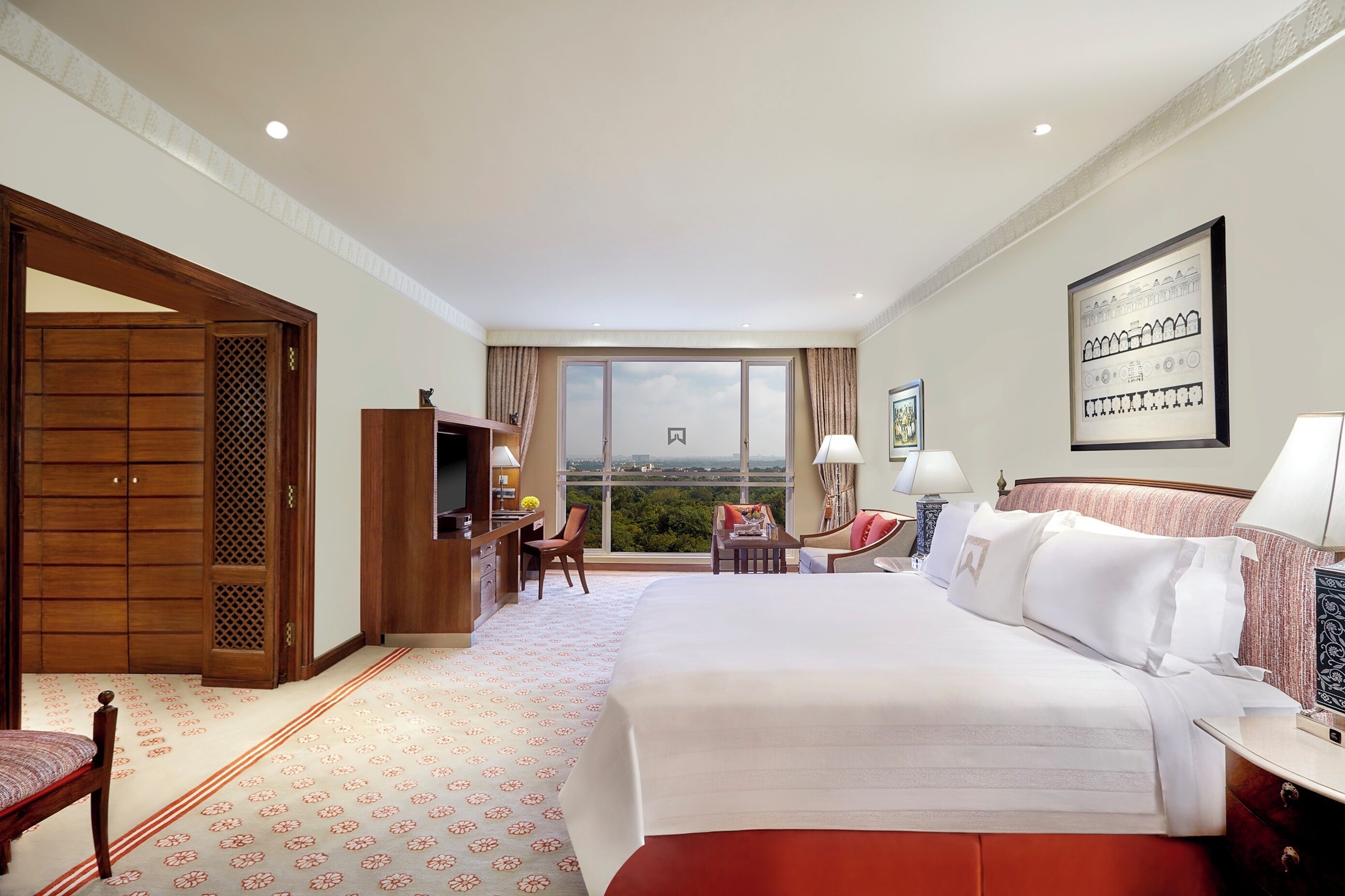 A hotel room with a large bed, a desk with a chair, a small seating area with a view, and a wardrobe.