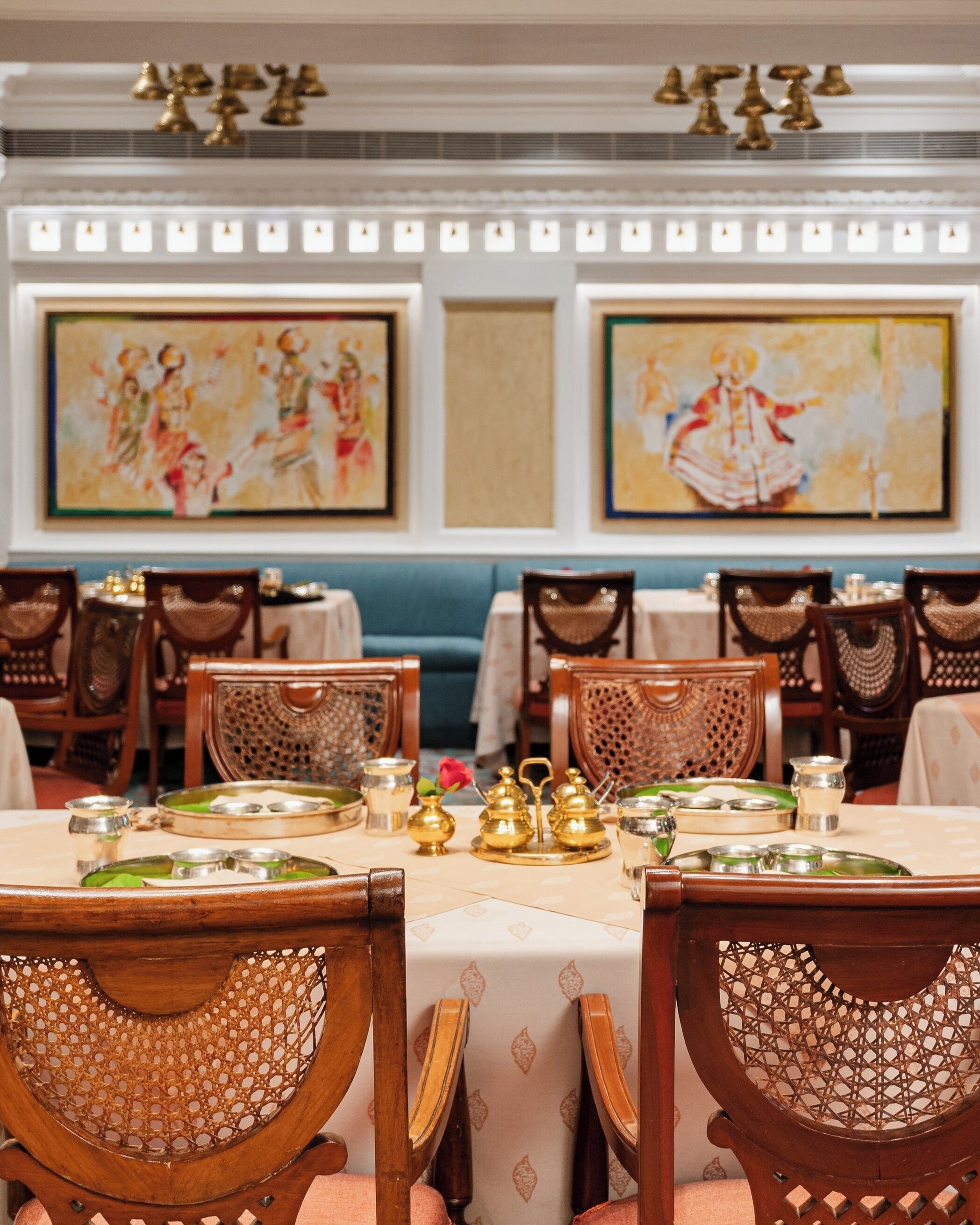 A dining area with wooden chairs and tables, brass serving sets, and framed artwork on the walls.