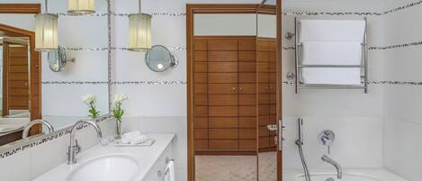 A modern bathroom with two sinks, a bathtub, and a wooden door leading to a shower area.
