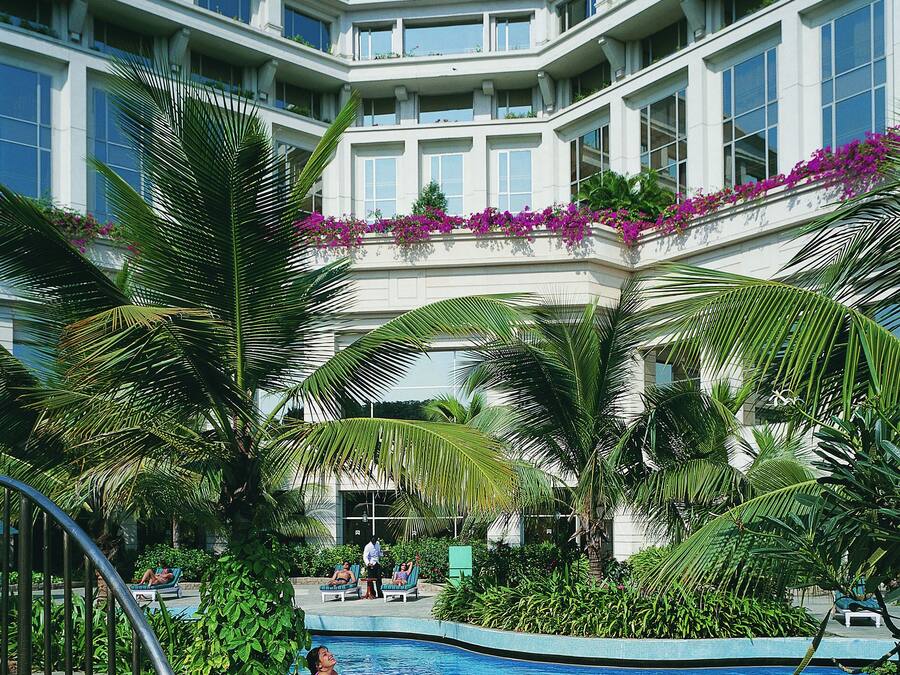 A hotel with a swimming pool surrounded by lush greenery and palm trees.