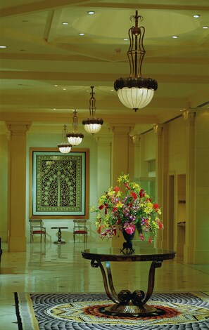 A lobby with a large decorative screen, a floral centerpiece on a table, and multiple hanging chandeliers.